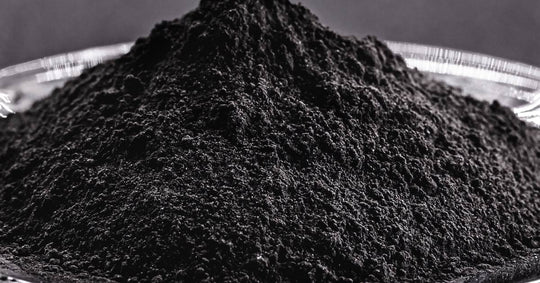 A large pile of black powder, up close, sitting on a round glass dish in front of a large gray wall.