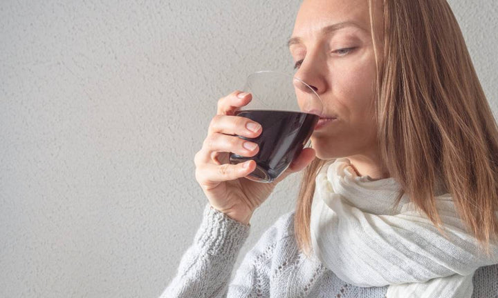 A blonde middle-aged woman drinking out of a clear glass. Inside the glass is a brown liquid consisting of humic acid.